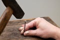 Male hand with stitches on fingers fixing the nail on the wood and hitting it with a hammer