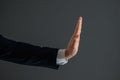 Male hand in a suit shows the palm of the stop gesture on a gray background. Stop concept, close-up