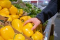 A male hand takes a yellow pepper from a box of peppers in a supermarket.