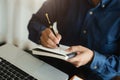 Male hand taking notes on a notebook handwritten note writing business schedule and use a laptop computer at the office desk Royalty Free Stock Photo