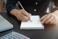 Male hand taking notes on a notebook handwritten note writing business schedule and use a laptop computer at the office desk Royalty Free Stock Photo