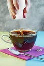 Male hand throwing sugar substitute pills into a cup of coffee and splash on yellow and blue podium Royalty Free Stock Photo