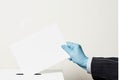 Male hand wearing blue protective latex glove placing ballot paper in vote box