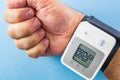 Male hand wearing white and grey wrist blood pressure monitor on blue background Royalty Free Stock Photo