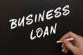 Male hand writes in chalk the words BUSINESS LOAN on a black board
