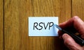 Male hand writes the words `RSVP` on a white card. Wooden table. Business concept, copy space