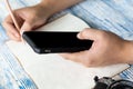 Male hand writing notepad and holding Smartphone on the lightblue table, Selective focus travel planing concept Royalty Free Stock Photo