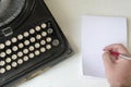 A male hand writing on a white checkered paper with a red pen next to an old wrecked black typewriter Royalty Free Stock Photo