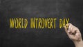 Male hand writing the words World Introvert Day on chalkboard