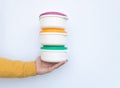 Male hand in a yellow sweater holding several colourful plastic food containers on each other. Isolated on white background. Royalty Free Stock Photo