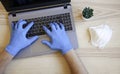 Male hands in blue protective gloves working on modern laptop. Specialist doctor in blue latex gloves. Medical mask is on the desk