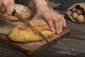 Male hands with a bread knife cut fresh crispy baguette on a wooden board. Sliced traditional french bread. Close-up Royalty Free Stock Photo