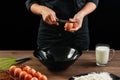 Male hands chef chefs break the egg on a wooden brown table in a black bowl. Black background. The concept of cooking food. Close- Royalty Free Stock Photo