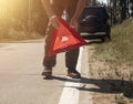 Male hands closeup putting red triangle caution sign on road side near broken car in summer Royalty Free Stock Photo