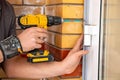 Male hands of construction worker tighten and fix screws and self-tapping screw with electric cordless screwdriver for home