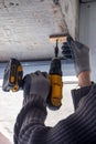 Male hands of construction worker tighten and fix screws and self-tapping screw with electric cordless screwdriver for home