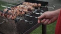 Male hands cook shish kebab on grill outside.