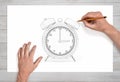 Male hands drawing a retro alarm block with two bells using a pencil on a white paper in close view. Royalty Free Stock Photo