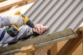 Male hands in gloves with a screwdriver screw the roofing sheet to the roof.