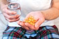 Male hands hold a glass of water and a handful of Omega-3 fatty acid capsules. Taking vitamins and supplements. Close-up