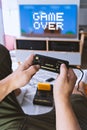 Male hands hold joystick video-game console next blue TV-screen with text Game Over. First-person view