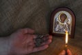 Male Hands hold a pectoral cross and a burning candle in front of a Christian icon