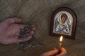 Male Hands hold a pectoral cross and a burning candle in front of a Christian icon