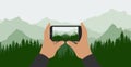 Male hands hold phone and take picture of beautiful nature, landscape. Silhouette of green forest on background of mountains.