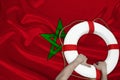 Male hands hold on to a white lifebuoy against the background of the silk national flag of Morocco, the concept of medical