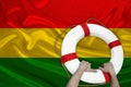 Male hands hold on a white life buoy against the background of the silk national flag of bolivia, the concept of medical insurance