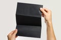 Male hands holding a black booklet triple sheet of paper. Isolated on gray background. Closeup
