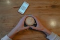 Top view of phone with kuar code and hands holding a cup of coffee in a cafe