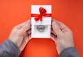 Male hands holding a half opened white gift box with a steel model of a human brain inside and a red bow with a ribbon on the