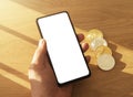 Male hands holding mobile phone with screen for app mock up and crypto currency coins in hand over wooden table