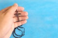 Male hands holding and praying the rosary or scapular in sky blue background.