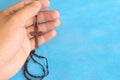 Male hands holding and praying the rosary or scapular in sky blue background. Royalty Free Stock Photo