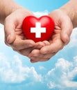 Male hands holding red heart with white cross Royalty Free Stock Photo