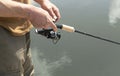 Male hands holding and rotating spinning reel rod, spoon-bait and fishing over river, closeup Royalty Free Stock Photo