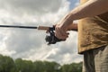 Male hands holding spinning reel rod or spoon-bait and fishing for trout, closeup. Sky and trees on background Royalty Free Stock Photo