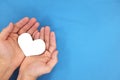 Male hands holding a white heart in blue background top view. Kindness, charity and compassion concept.