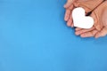 Male hands holding a white heart in blue background top view. Kindness, charity and compassion concept.