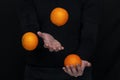 Male hands juggle with fresh oranges on a dark background