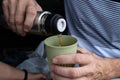 Male hands pour coffee or tea from a thermos into a reusable glass. Zero waste concept