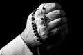 Male hands praying holding a rosary with Jesus Christ in the cross or Crucifix on black background. Royalty Free Stock Photo