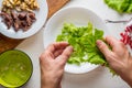 Male hands tearing lettuce leaves over a plate.