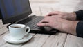 Male hands are typing on a laptop keyboard with a cup of coffee on a wooden antique table. Programmer, online education Royalty Free Stock Photo