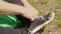 Male hands undoing shoelaces on sneakers while outdoor rest. Man unties laces on sneakers sitting on meadow grass.