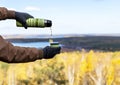 Male hands in warm gloves pour hot tea from thermos on rock against the backdrop of beautiful autumn view of lake and forest with Royalty Free Stock Photo