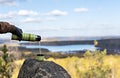 Male hands in warm gloves pour hot tea from thermos on rock against the backdrop of beautiful autumn view of lake and forest with Royalty Free Stock Photo