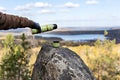 Male hands in warm gloves pour hot tea from thermos on rock against the backdrop of beautiful autumn view of lake and forest with Royalty Free Stock Photo